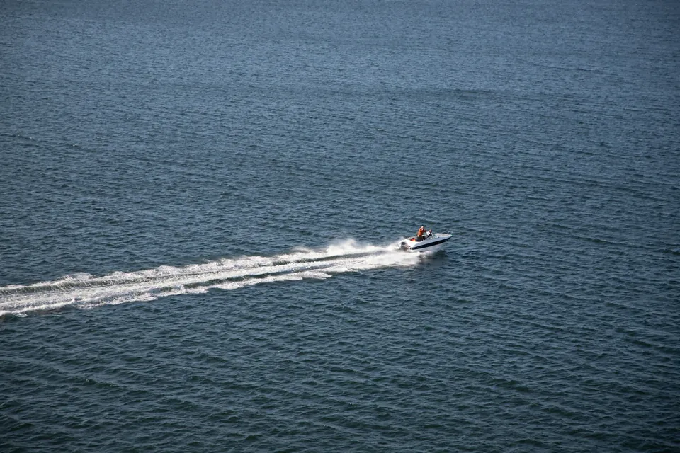 White motorboat crossing open water with a long wake